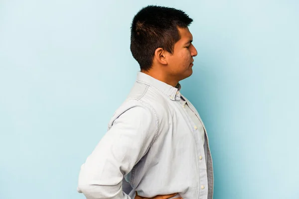 青い背景に孤立した若いヒスパニック系の男が腰痛に苦しんでいる — ストック写真