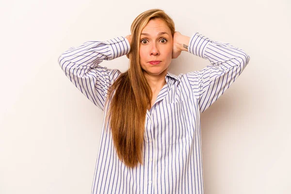 Beyaz arka planda izole edilmiş genç beyaz bir kadın. Kulakları kulaklarıyla kapatıyor. Çok fazla ses duymamaya çalışıyor..