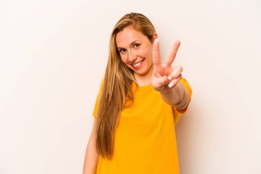 Beyaz arka planda izole edilmiş genç beyaz kadın neşeli ve kaygısız parmakları olan bir barış sembolü gösteriyor..