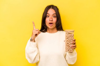 Sarı arka planda izole edilmiş nohut kavanozunu tutan genç İspanyol kadının bir fikri var, ilham verici bir kavram..