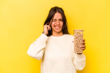 Elinde nohut kavanozu tutan genç İspanyol kadın sarı arka planda izole edilmiş kulakları elleriyle kapatıyor..