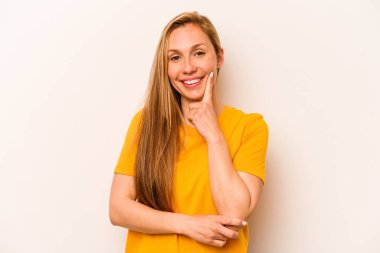 Beyaz arka planda izole edilmiş genç beyaz kadın mutlu ve kendinden emin gülümsüyor, elleriyle çenesine dokunuyor..