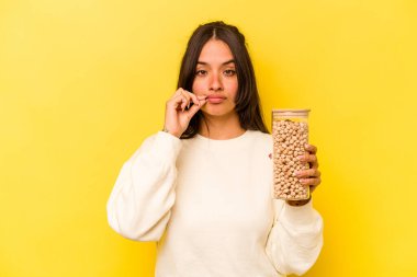 Sarı arka planda izole edilmiş nohut kavanozunu tutan genç İspanyol kadın dudaklarında bir sır saklıyor..