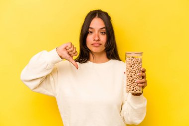 Sarı arka planda izole edilmiş nohut kavanozu tutan İspanyol genç bir kadın hoşlanmadığı bir jest gösteriyor. Anlaşmazlık konsepti.