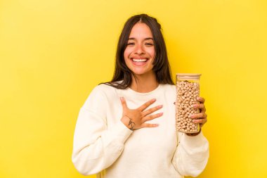 Sarı arka planda izole edilmiş nohut kavanozunu tutan genç İspanyol kadın kahkahalar atıyor..