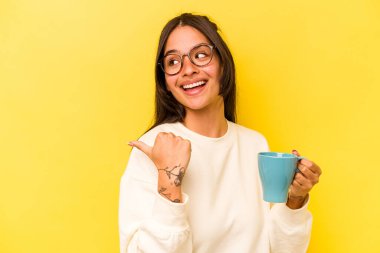 Sarı arka planda bir kupa tutan genç İspanyol kadın parmak uzakta, gülüyor ve kaygısız..