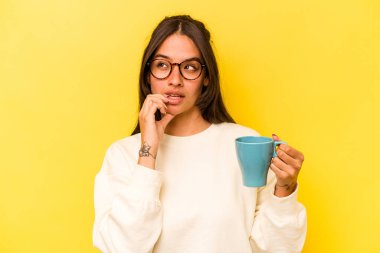 Sarı arka planda izole edilmiş bir kupa tutan genç İspanyol kadın bir şeyin fotokopi odasına baktığını düşünerek rahatladı..