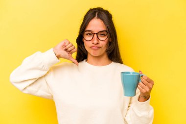 Sarı arka planda izole edilmiş bir kupa tutan genç İspanyol kadın gururlu ve kendinden emin hissediyor..