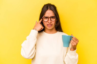 Sarı arka planda bir kupa tutan genç İspanyol kadın işaret parmağıyla hayal kırıklığı gösteriyor..