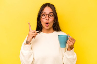 Sarı arka planda izole edilmiş bir kupa tutan genç İspanyol kadının bir fikri var, ilham verici bir kavram..