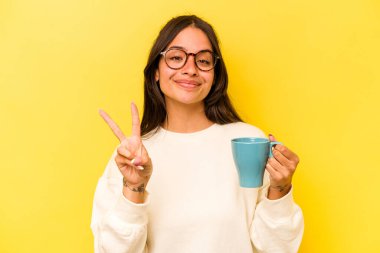 Sarı arka planda iki numarayı parmaklarıyla gösteren bir kupa tutan genç İspanyol kadın..