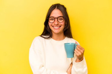 Sarı arka planda bir kupa tutan genç İspanyol kadın gülüyor ve eğleniyor..