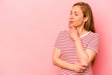 Pembe arka planda soyutlanmış beyaz bir kadın şüpheli ve şüpheci bir ifadeyle yana bakıyor..