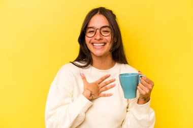 Sarı arka planda saklanmış bir kupa tutan genç İspanyol kadın kahkahalarla gülüyor..