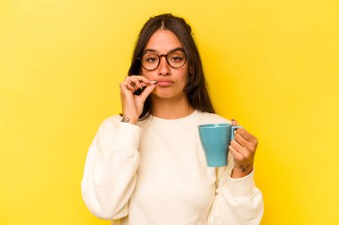Sarı arka planda, dudakları dudaklarında bir sırrı saklayan bir kupa tutan genç İspanyol kadın..