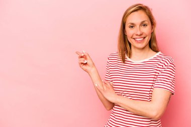 Pembe arka planda izole edilmiş genç beyaz kadın işaret parmağıyla işaret ederek gülümsüyor..