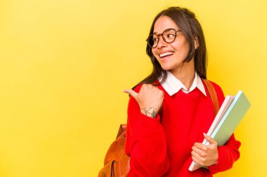 Genç İspanyol öğrenci, sarı arka planda izole edilmiş, başparmak uzakta, gülen ve kaygısız..