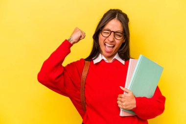 Genç İspanyol öğrenci, sarı arka planda izole edilmiş zafer sonrası yumruğunu kaldıran, kazanan konsept..