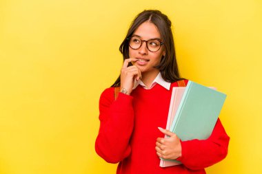Genç İspanyol öğrenci, sarı arka planda izole edilmiş. Rahatlamış, fotokopi odasına bakan bir şey düşünüyor..