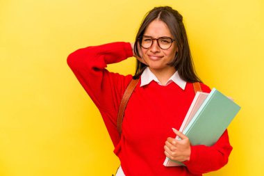 Genç İspanyol öğrenci, sarı arka planda izole edilmiş. Kafasının arkasına dokunuyor, düşünüyor ve bir seçim yapıyor..