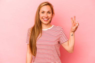 Pembe arka planda izole edilmiş genç beyaz kadın zafer işareti gösteriyor ve gülümsüyor..