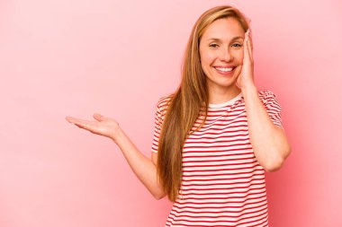 Pembe arka planda izole edilmiş genç beyaz kadın avuç içinde fotokopi alanı tutuyor, el üstünde tutuyor. Şaşırmış ve mutlu..