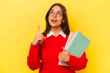 Sarı arka planda izole edilmiş, ağzı açık, üst tarafı işaret eden genç İspanyol bir kadın..