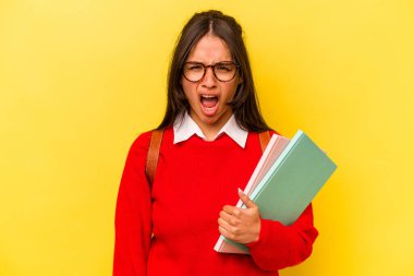 Sarı arka planda izole edilmiş genç İspanyol bir kadın çok sinirli ve agresif çığlıklar atıyor..