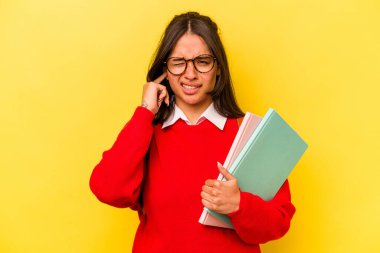 Sarı arka planda izole edilmiş, kulaklarını elleriyle kapatan genç İspanyol öğrenci kadın..