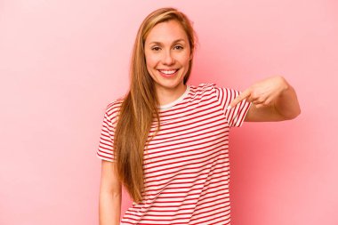 Pembe arka planda izole edilmiş genç beyaz bir kadın gömlek fotokopisini elle gösteriyor, gururlu ve kendinden emin.