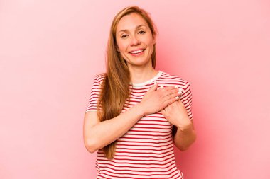 Pembe arka planda izole edilmiş genç beyaz bir kadın, dostane bir ifadeye sahip, avuçlarını göğsüne bastırıyor. Aşk konsepti.