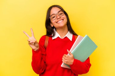 Genç İspanyol öğrenci, sarı arka planda izole edilmiş neşeli ve kaygısız parmakları olan barış sembolü gösteriyor..