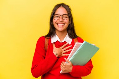 Sarı arka planda izole edilmiş genç İspanyol bir kadın elini göğsüne bastırarak kahkahalar atıyor..