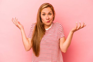 Pembe arka planda izole edilmiş genç beyaz kadın sorgulama sırasında omuz silkiyor ve şüphe duyuyor..