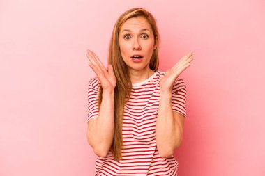 Pembe arka planda izole edilmiş genç beyaz kadın şaşırmış ve şok olmuş..