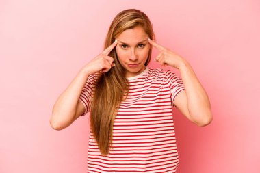 Pembe arka planda izole edilmiş genç beyaz kadın bir göreve odaklanmış, parmaklarını işaret ediyor..