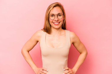 Pembe arka planda izole edilmiş beyaz bir kadın. Kendine güveni tam. Kalçalarını tutuyor..