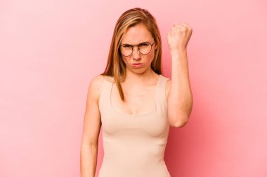 Pembe arka planda izole edilmiş genç beyaz kadın yumruğunu kameraya gösteriyor, agresif yüz ifadesi..