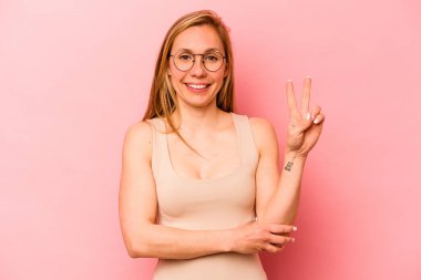 Pembe arka planda izole edilmiş genç beyaz kadın iki numarayı parmaklarıyla gösteriyor..