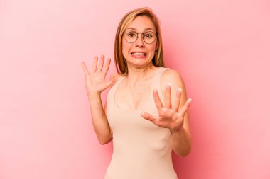 Pembe arka planda izole edilmiş genç beyaz kadın yakın bir tehlike nedeniyle şoka uğruyor.