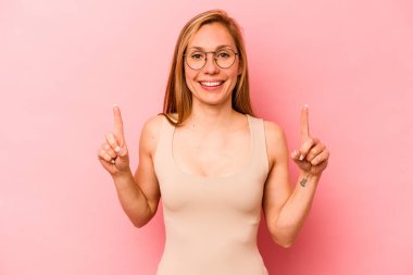 Pembe arka planda izole edilmiş genç beyaz kadın iki parmağı da boş bir alan gösteriyor..