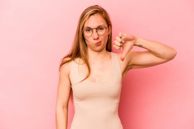 Pembe arka planda izole edilmiş genç beyaz kadın baş parmağını aşağı gösteriyor, hayal kırıklığı konsepti..