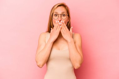 Pembe arka planda izole edilmiş genç beyaz kadın şok olmuş, ağzı ellerle kaplanmış, yeni bir şey keşfetmeye hevesli..