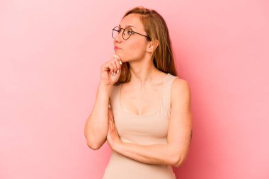 Genç, beyaz bir kadın pembe arka planda izole edilmiş düşünüyor ve yukarı bakıyor, yansıtıyor, düşünüyor, fantezi kuruyor..