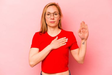 Pembe arka planda izole edilmiş genç beyaz kadın yemin ediyor, elini göğsüne koyuyor..