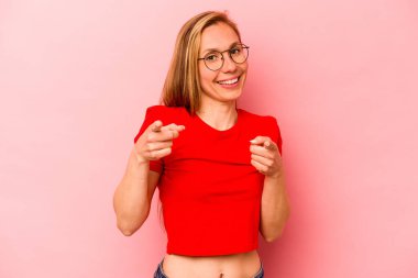 Pembe arka planda izole edilmiş genç beyaz kadın parmaklarıyla ön tarafı işaret ediyor..