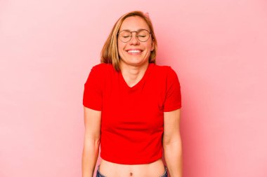 Pembe arka planda izole edilmiş genç beyaz kadın gülüyor ve gözlerini kapıyor, rahatlamış ve mutlu hissediyor..