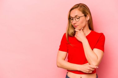 Pembe arka planda soyutlanmış beyaz bir kadın şüpheli ve şüpheci bir ifadeyle yana bakıyor..