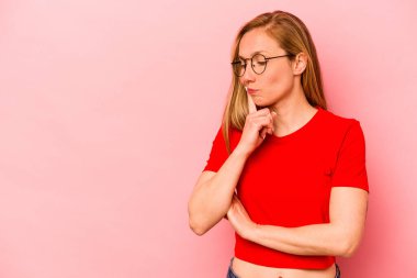 Pembe arka planda soyutlanmış beyaz bir kadın şüpheli ve şüpheci bir ifadeyle yana bakıyor..