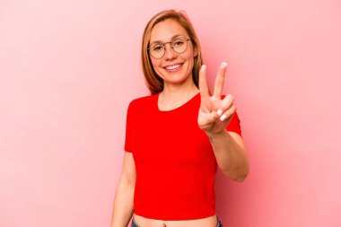 Pembe arka planda izole edilmiş genç beyaz kadın zafer işareti gösteriyor ve gülümsüyor..